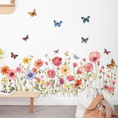 a white wall with flowers and butterflies painted on it, along with a bench in the foreground