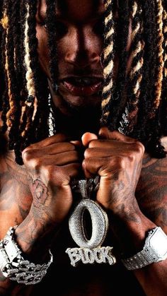 a man with dreadlocks holding his hands to his chest and wearing a necklace