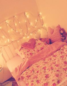 an unmade bed with white sheets and pink flowers on it, surrounded by fairy lights