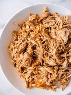 shredded chicken in a white bowl on a marble counter top, ready to be eaten