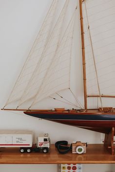 a model sailboat on a wooden shelf with other toy cars and trucks around it