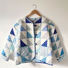 a blue and white quilted jacket hanging on a wooden hanger next to a wall