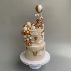 a three tiered cake decorated with balloons and a teddy bear