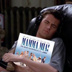 a man sitting in a chair holding up a book with the title mamma mia on it