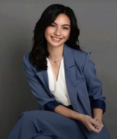 a woman in a blue suit and white shirt sitting on a chair with her legs crossed