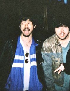 three young men standing next to each other in front of a dark room with one pointing at the camera