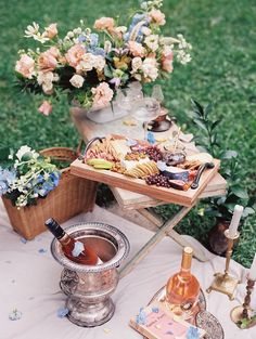 a table topped with wine and food on top of a grass covered field next to flowers