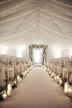 an indoor wedding venue with candles and flowers on the aisle, surrounded by white draping