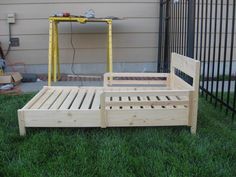 a wooden bed frame sitting on top of green grass in front of a fenced yard