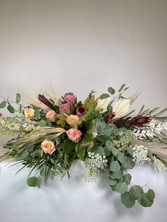 an arrangement of flowers and greenery on a white surface