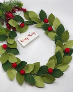 a christmas wreath made out of felt with red berries and green leaves on the front