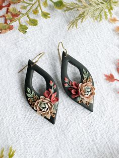 two pairs of earrings with flowers on them sitting on top of a white cloth covered surface