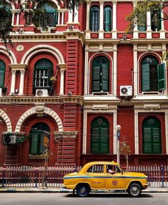 a yellow taxi cab is parked in front of an old red building with green shutters