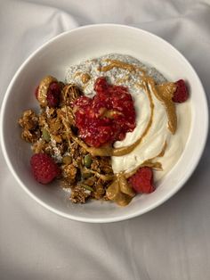 a white bowl filled with granola, yogurt and raspberries