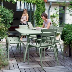 two women sitting at an outdoor table with laptops on it and one woman standing in the background