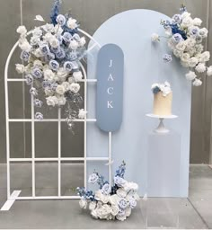 a white and blue wedding cake with flowers on display in front of a backdrop that says jack