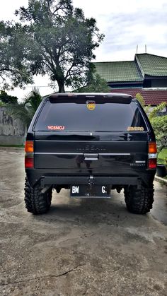 a black suv parked on top of a dirt covered parking lot next to a tree