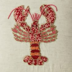 an embroidered lobster on a white cloth with pink thread and bead work, in the shape of a cross stitch pattern