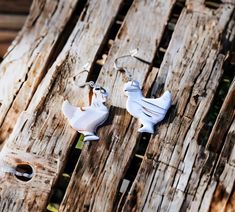 two white bird shaped earrings sitting on wooden planks