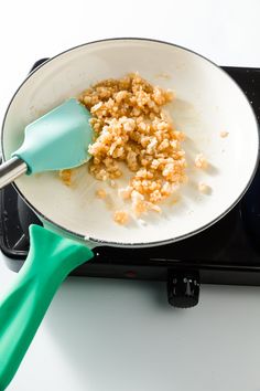 a frying pan filled with food sitting on top of a stove next to a green spatula