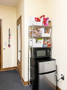 a room with a microwave, refrigerator and other items on the shelves in front of the door