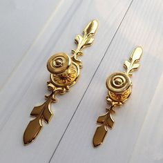 two gold earrings with leaves on them are sitting on a white surface and one has a button in the middle