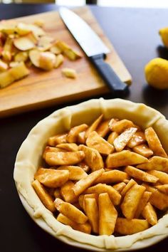 a pie crust with apples in it on a table next to cutting board and knife