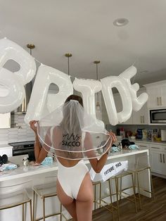 the back of a woman in a white bodysuit holding up balloons that say bride