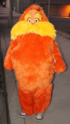 a man in an orange and yellow costume standing on the sidewalk with his hands behind his back