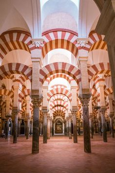 the inside of a building with columns and arches on both sides that are decorated in red, white and orange stripes