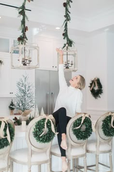 a woman sitting on top of a kitchen counter with wreaths hanging from the ceiling