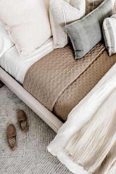 a bed with several pillows and slippers on the floor next to it's headboard