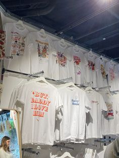 there are many t - shirts hanging up on the wall in front of a woman