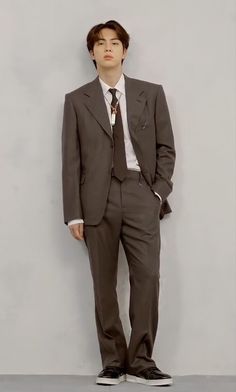 a young man in a suit and tie standing against a gray wall with his hands in his pockets