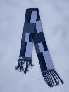 a blue and grey scarf laying on top of snow covered ground with fringes around it