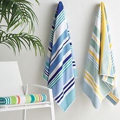 two towels hanging on the wall next to a chair and potted plant in a white room