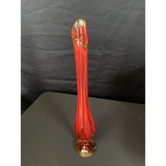 a red glass vase sitting on top of a black table next to a gray wall