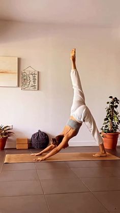 a woman is doing a yoga pose in front of a wall with potted plants