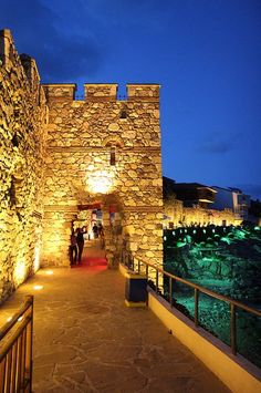 a stone building lit up at night with people walking down the walkway in front of it