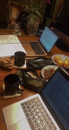 two laptops are sitting on a table with papers and coffee mugs next to them