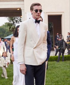 a man in a tuxedo and sunglasses standing on the grass with people behind him