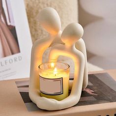 a candle that is sitting on top of a box next to a book with an image of two people holding each other