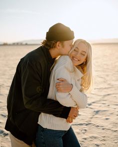 a man and woman hugging each other on the beach