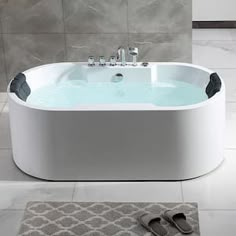 a white bath tub sitting on top of a bathroom floor next to a rug and sink