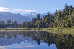 a lake surrounded by trees with mountains in the background