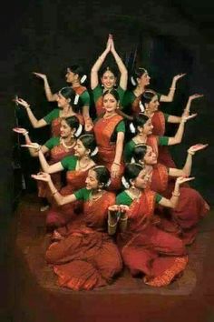 a group of women in red and green dresses are doing yoga poses with their hands up