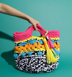 a woman's hand holding a multicolored crocheted bag with tassels