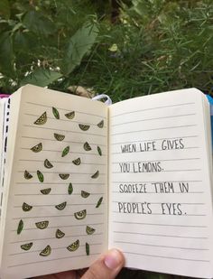 someone is holding an open book in their hand with words written on it and green leaves