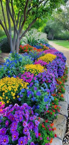 the colorful flowers are growing on the side of the stone wall in the garden area