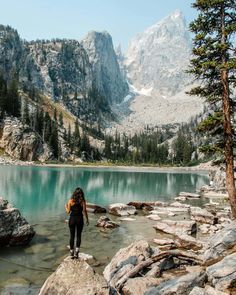 a woman standing on rocks near a lake with mountains in the background